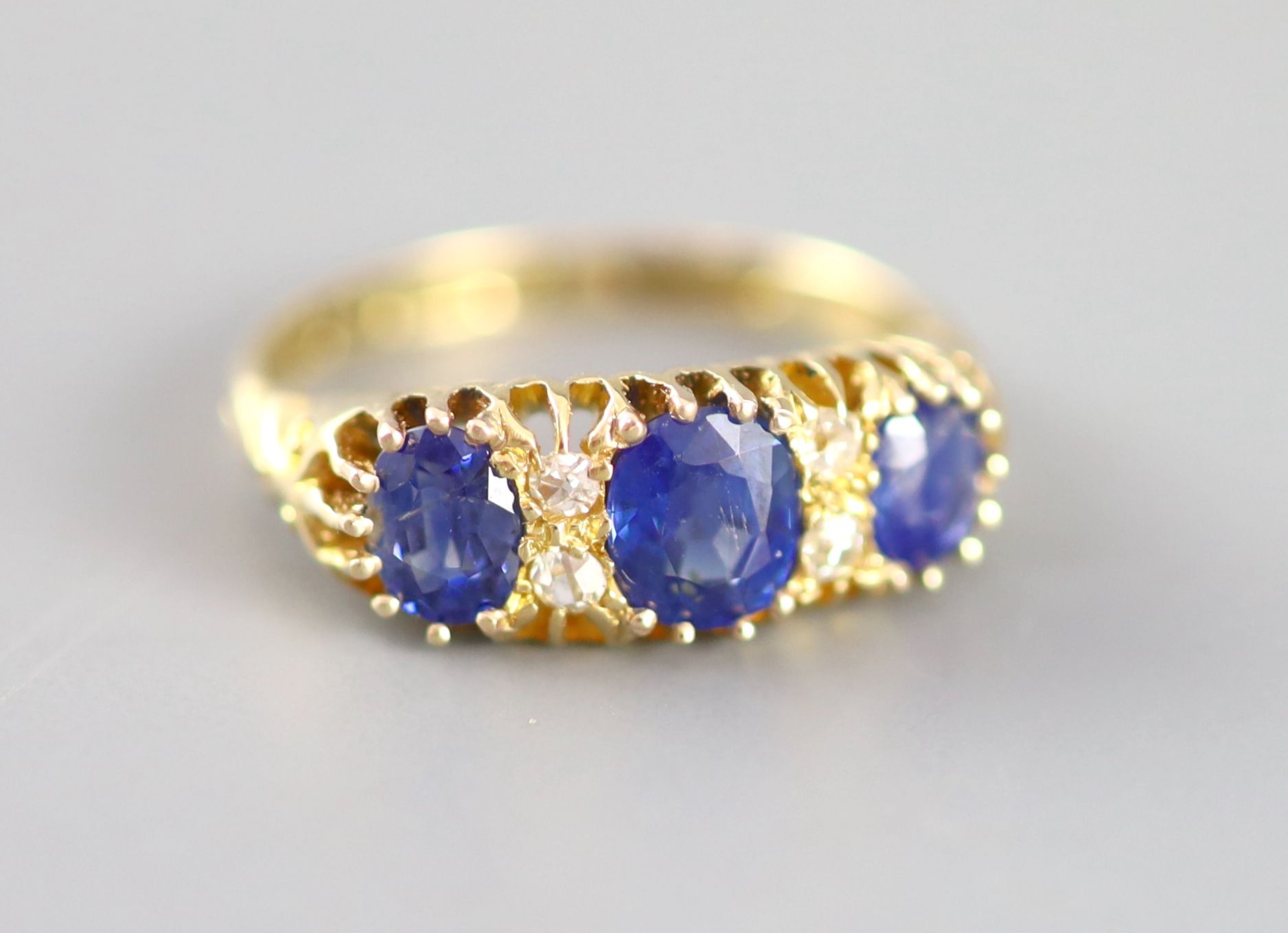 An Edwardian 18ct gold and three stone sapphire set half hoop ring with diamond chip spacers